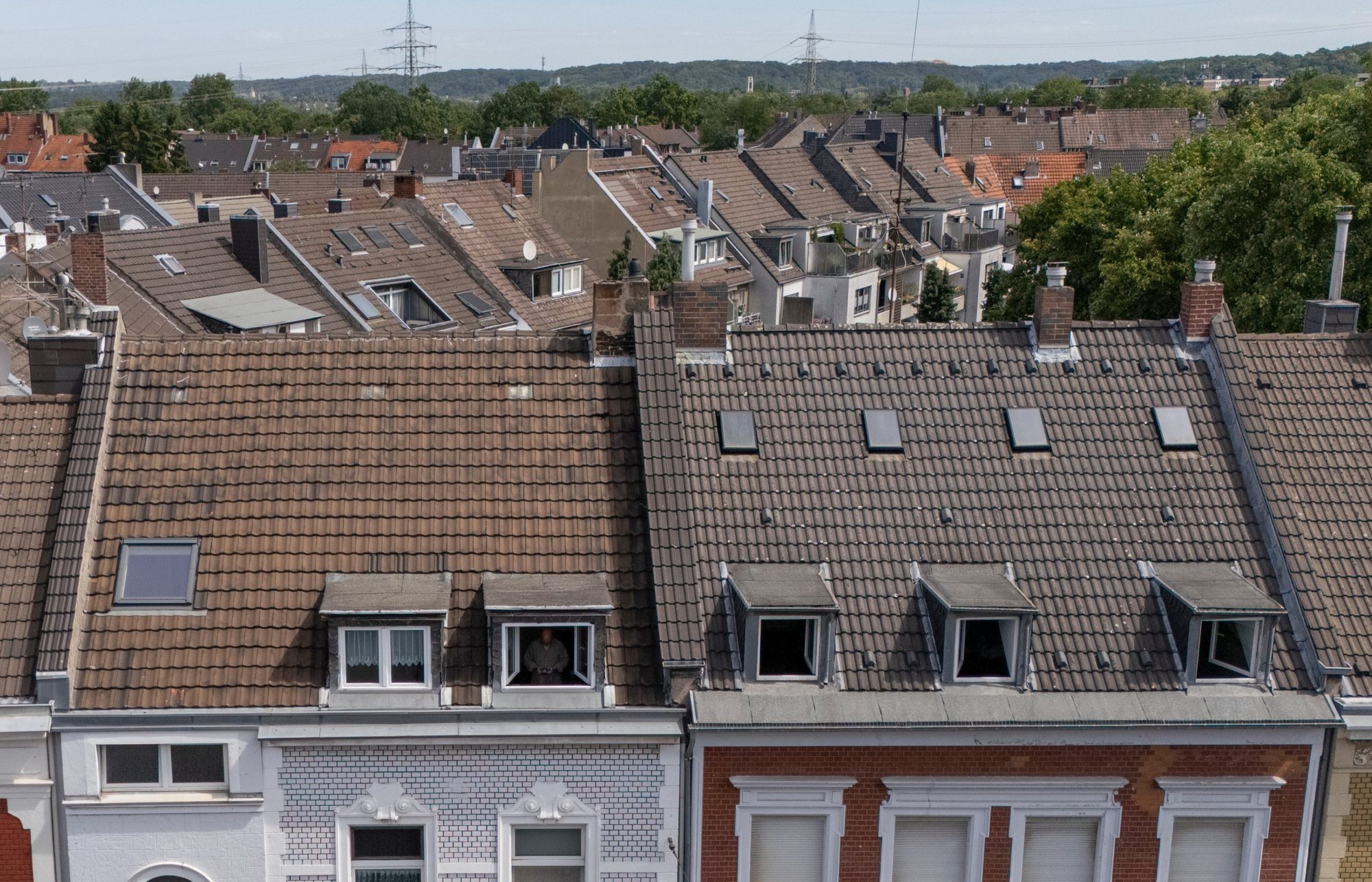 Drohnenaufnahme einer Häuserzeile mit Ziegeldächern, Gauben, Kaminen und Dachfenstern