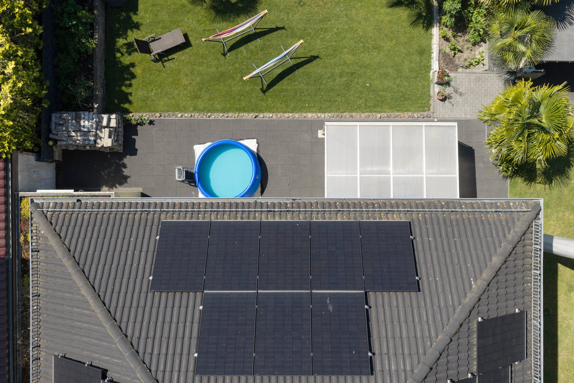 Nahaufnahme von oben auf ein Ziegeldach mit Photovoltaik-Modulen, Garten und Terrasse